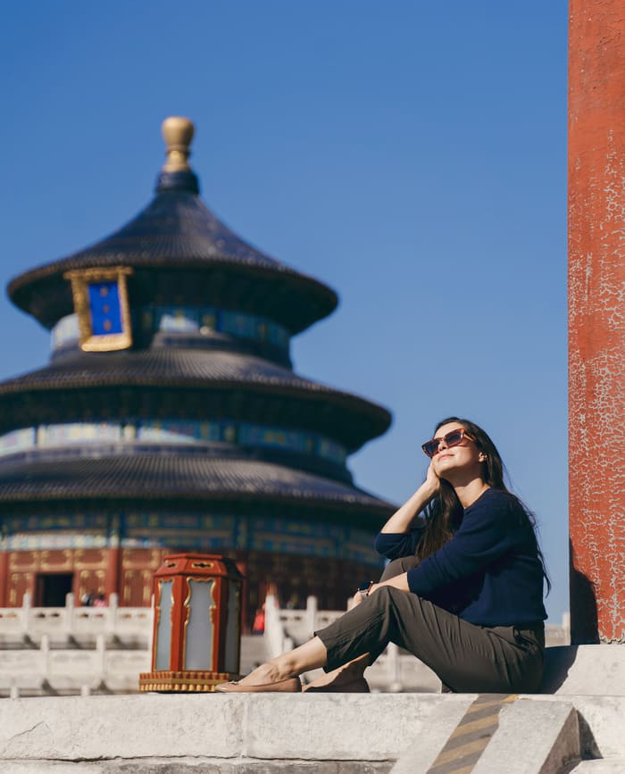 Mujer turista sentada en primer plano mirando hacia el cielo, detrás un templo Chino