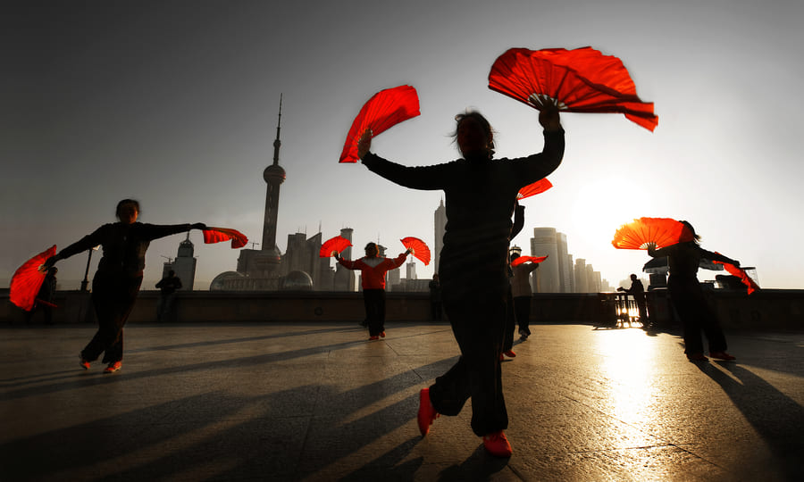 Personas bailando baile típico de China. Se ven siluetas y unos abanicos grandes en sus manos