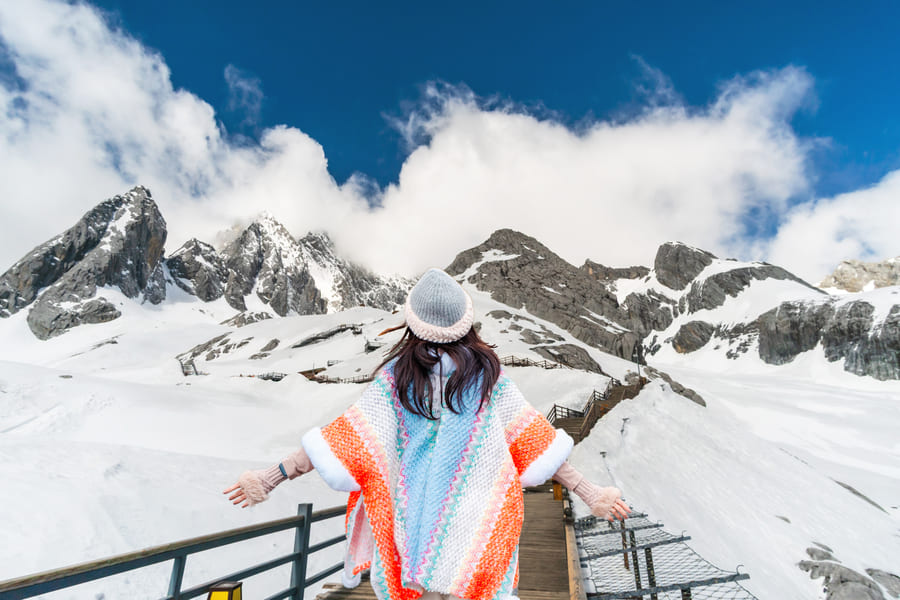 Mujer de espaldas con gorro y un abrigo de invierno. Al fondo un paisaje de montañas con nueve en Yulongshang